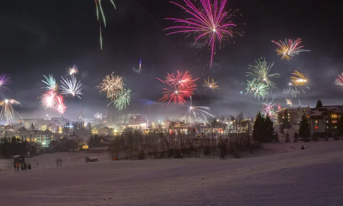 Colorful fireworks light up the sky over a snowy alpine village at night